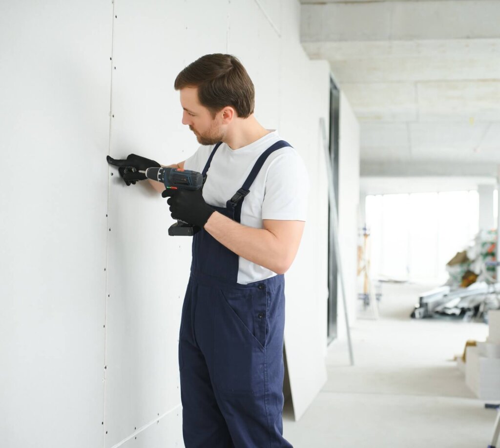 Worker builder installs plasterboard drywall at a construction
