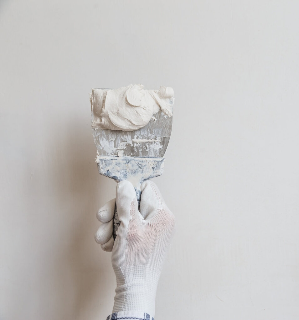 Worker in white gloves performs plastering of the walls of the room